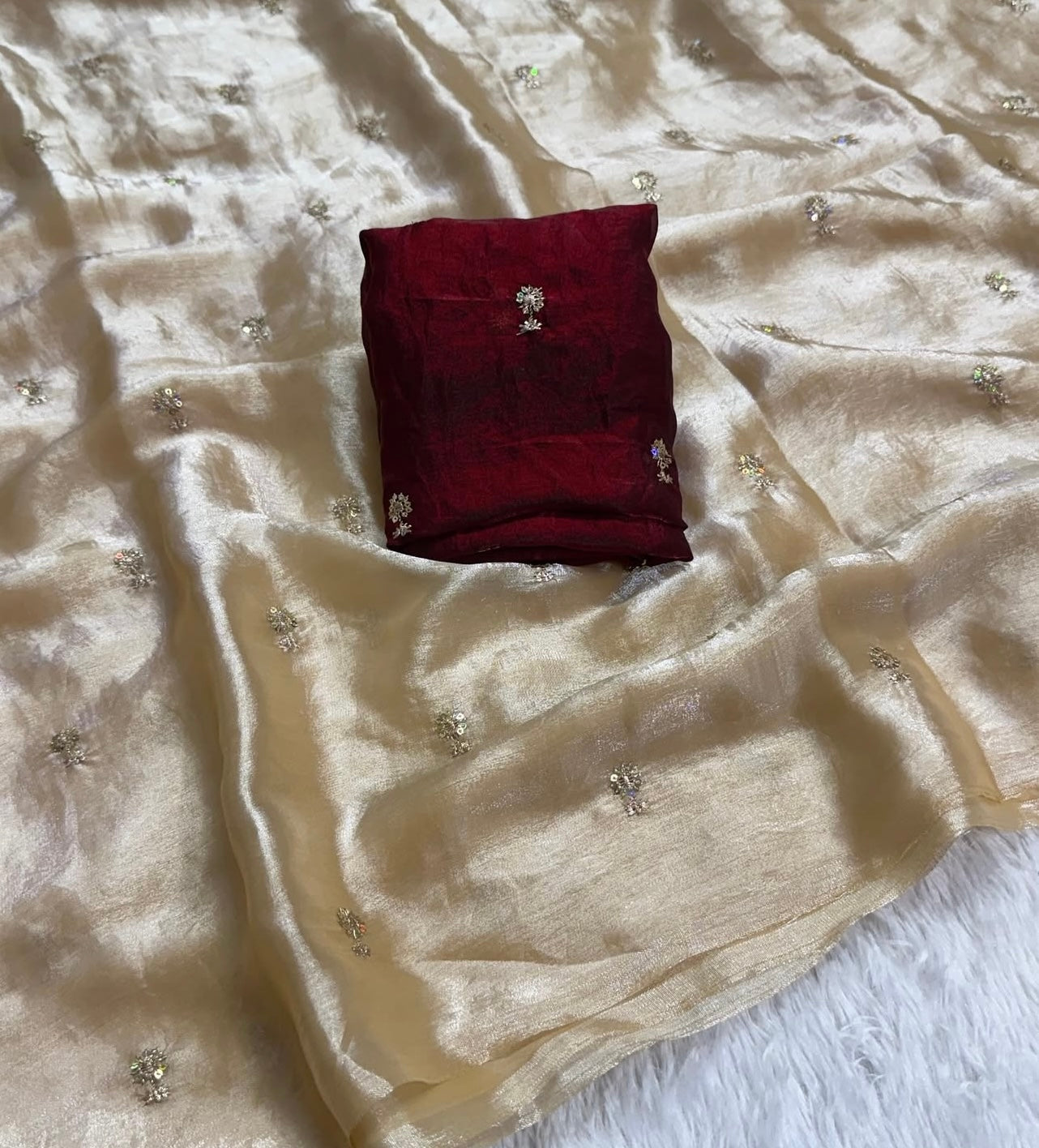 A Soft Beige Color Stardust Satin Saree Dual Shaded Sequins Jari Butti Work Allover the saree paired with Deep Maroon Color Sequins work Blouse