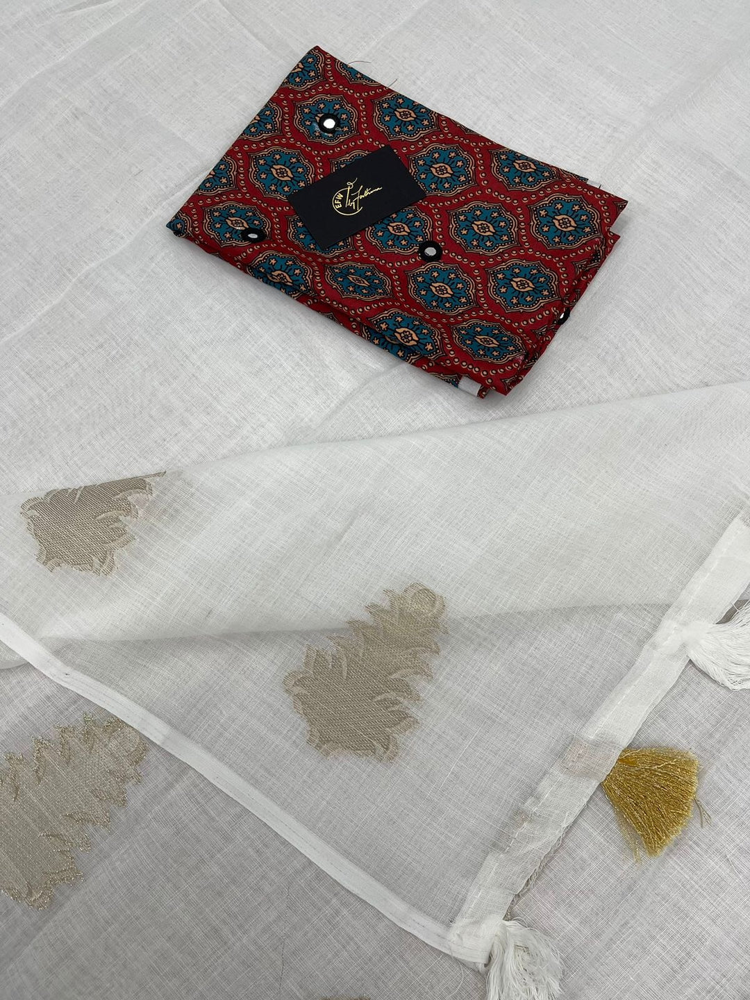 White LINEN Saree, featuring beautiful zari woven leaf design...pallu is adorned with cotton tassels...blouse is made of linen fabric with ajrakh style prints and foil mirror work