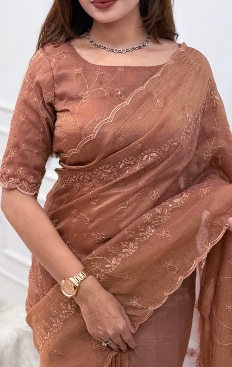 A woman wearing a warm brownish-rose saree with embroidered floral patterns and a matching blouse, shown in a close-up lifestyle shot.